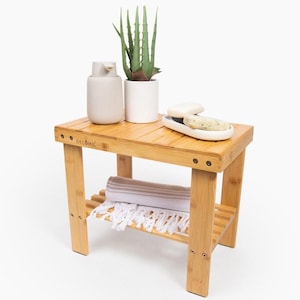 May include: A natural bamboo bathroom shelf with a white towel, a white soap dish with two bars of soap, a white ceramic soap dispenser, and a potted aloe vera plant.