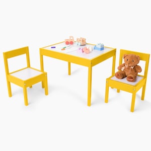 May include: A yellow children's table and two chairs set with a white whiteboard surface. The table is decorated with toy cars and blocks.