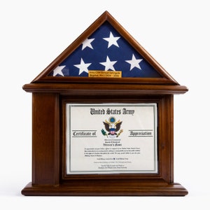 May include: A wooden flag display case with a blue and white American flag in the top section. Below is a certificate from the United States Army. The case has a dark brown finish and a rectangular shape.
