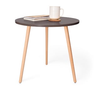 May include: A dark brown round side table with three light wood legs. A white mug and a stack of books are on the table.