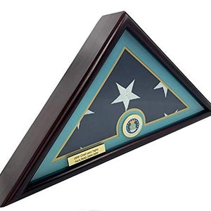 Könnte beinhalten: Eine hölzerne Schattenbox mit einer gefalteten amerikanischen Flagge darin. Die Flagge ist blau, weiß und rot mit einem goldenen Stern in der Mitte. Die Box hat eine goldene Plakette mit dem Text "USAF Chief Leon Wright, Iraq 2004-2005".
