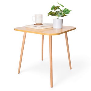 May include: A light wood end table with a rounded square top and four tapered legs. A white ceramic mug and a book are on the table, and a potted plant is to the right.