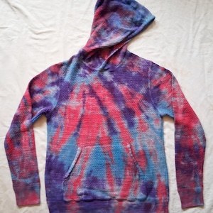 May include: A tie-dye hoodie in shades of pink, blue, and purple. The hooded sweatshirt has a kangaroo pocket and ribbed cuffs and hem. The fabric has a waffle-knit texture.