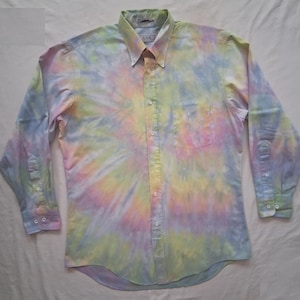 May include: A long-sleeve button-down shirt featuring a pastel tie-dye pattern in shades of light blue, soft yellow, and pale pink. The shirt includes a pointed collar, a front button placket, a single chest pocket, and buttoned cuffs.