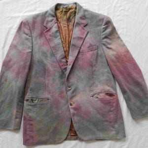 May include: A gray blazer with a tie-dye pattern in shades of pink, blue, and green. The blazer has a single button closure and two flap pockets.