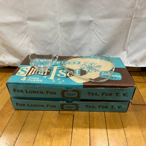 May include: A box set of four glass cups and plates, labeled "Smart Set" and "Indiana Glass". The box is brown with blue and white accents. The text on the box reads "For Lunch, For Tea, For T.V."