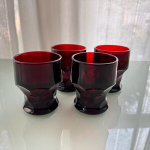 Könnte beinhalten: Vier rubinrote Glasbecher mit facettiertem Design. Die Gläser stehen auf einer weißen Oberfläche.
