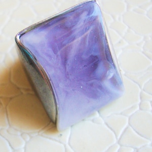 May include: A silver ring with a large, square-shaped, purple and white marbled stone.