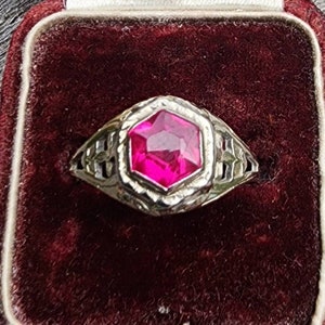May include: A silver ring with an ornate design and a large, faceted, dark pink gemstone.