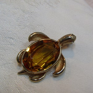 Puede incluir: Un broche de tortuga de tono dorado con una gran piedra de vidrio de color ámbar en el centro.