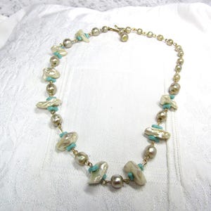 May include: A necklace featuring a sequence of round metallic gold beads and irregular off-white baroque pearls, interspersed with small, flat, circular turquoise-coloured spacer beads, connected by a thin gold-toned metal chain and clasp.