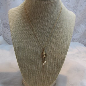 May include: A gold chain necklace with a pendant featuring two small, white pearls and a gold, leaf-shaped design.