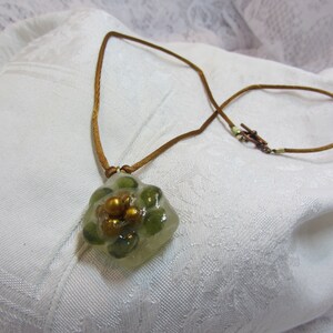 May include: A brown leather cord necklace with a green and gold resin flower pendant.