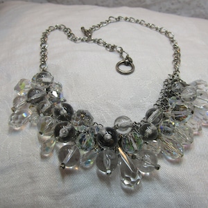May include: A silver chain necklace with a cluster of clear crystal beads. The beads are of various shapes and sizes, and some have a slight iridescent shimmer.