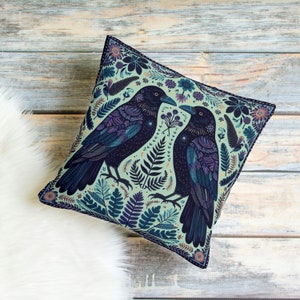 May include: A decorative throw pillow with a green background and a pattern of two black crows with intricate details, surrounded by floral and leafy designs.