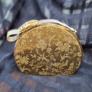 May include: A vintage, gold-toned, half-moon shaped purse with a floral and bird pattern. The purse has a white zipper and a gold clasp. The design is reminiscent of antique styles, suitable for special occasions.
