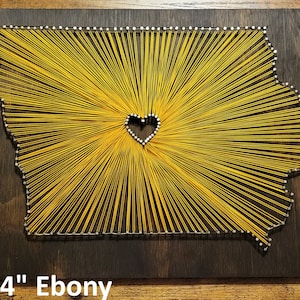 May include: A 12" x 14" string art piece in the shape of the state of Iowa with a heart in the center. The string art is on a dark wood background. The string is yellow.