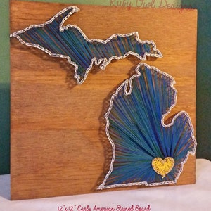 May include: String art of the state of Michigan on a 12" x 12" Early American Stained Board. The state is outlined in silver thread and filled in with blue, green, and yellow thread. A yellow heart is in the center of the state.