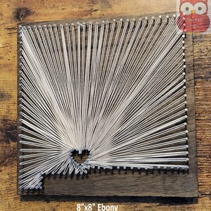May include: A white string art design on an 8" x 8" ebony wood square. The string art design is a geometric pattern with a hole in the center.