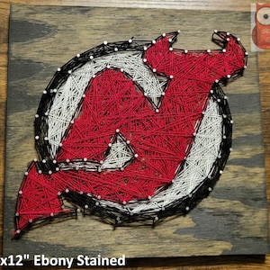 May include: A 12" x 12" wood sign with an ebony stain featuring a string art design of the New Jersey Devils logo. The logo is red, white, and black.