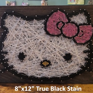 May include: String art of Hello Kitty on a dark wood background. The art is 8 inches by 12 inches and is stained true black.
