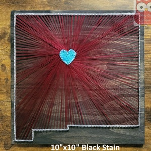 May include: String art of the state of New Mexico with a blue heart in the center. The art is on a 10" x 10" black stained wooden board.