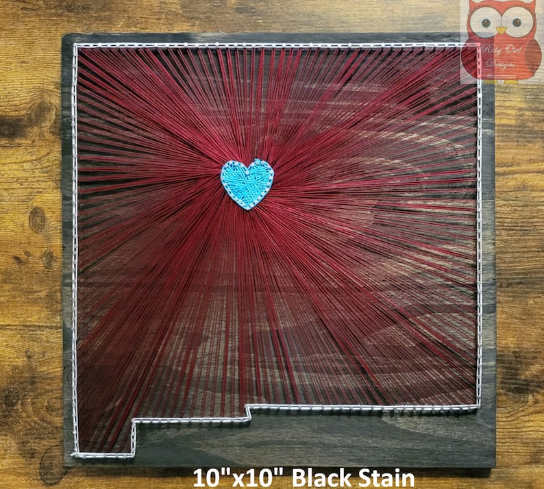 May include: String art of the state of New Mexico with a blue heart in the center. The art is on a 10" x 10" black stained wooden board.