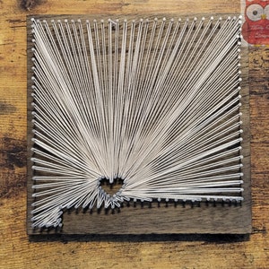 May include: A white string art piece in the shape of the state of Arizona on a dark brown wooden background.