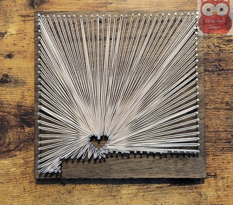 May include: A white string art piece in the shape of the state of Arizona on a dark brown wooden background.