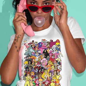 May include: A white t-shirt with a colorful graphic print of cartoon characters. The graphic features a variety of female characters from popular animated shows and movies.