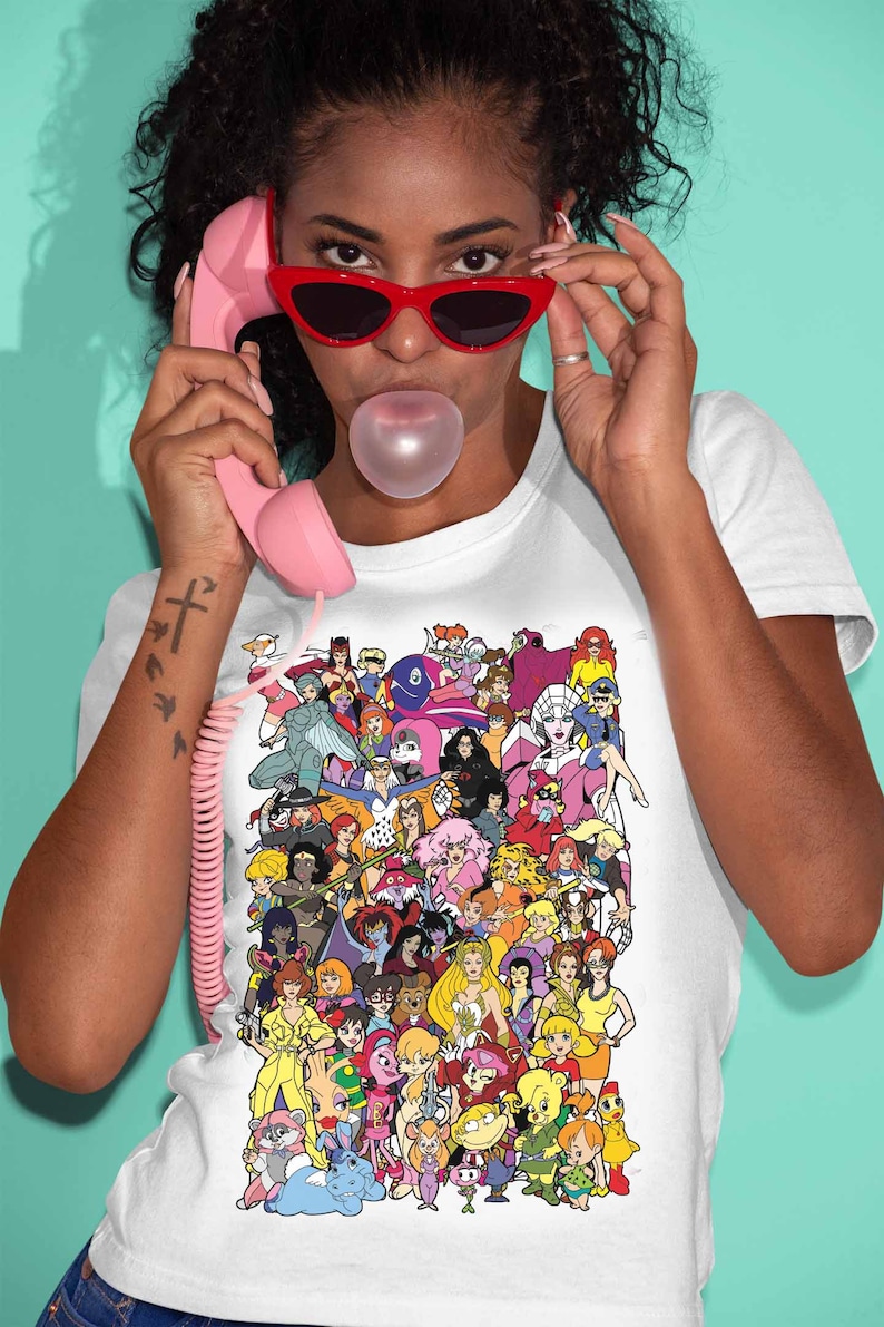 May include: A white t-shirt with a colorful graphic print of cartoon characters. The graphic features a variety of female characters from popular animated shows and movies.