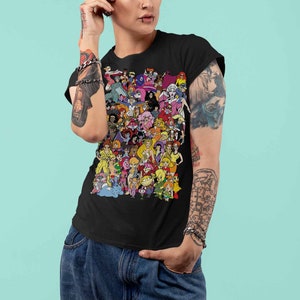 May include: A black t-shirt with a colorful graphic print of cartoon characters. The characters are all female and are wearing different outfits. The shirt is being worn by a person with tattoos on their arms.