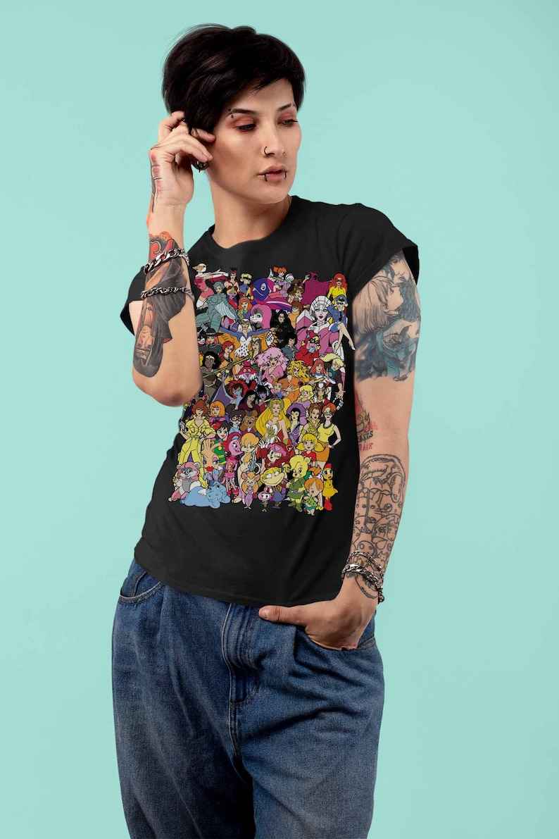 May include: A black t-shirt with a colorful graphic print of cartoon characters. The characters are all female and are wearing different outfits. The shirt is being worn by a person with tattoos on their arms.