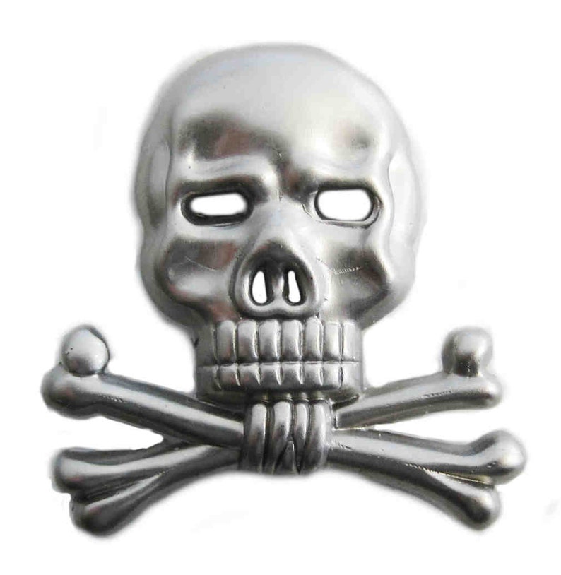 May include: A silver-colored skull and crossbones emblem. The skull has empty eye sockets, a nose cavity, and a detailed jawline. The crossbones are positioned beneath the skull, creating a classic pirate or gothic design.