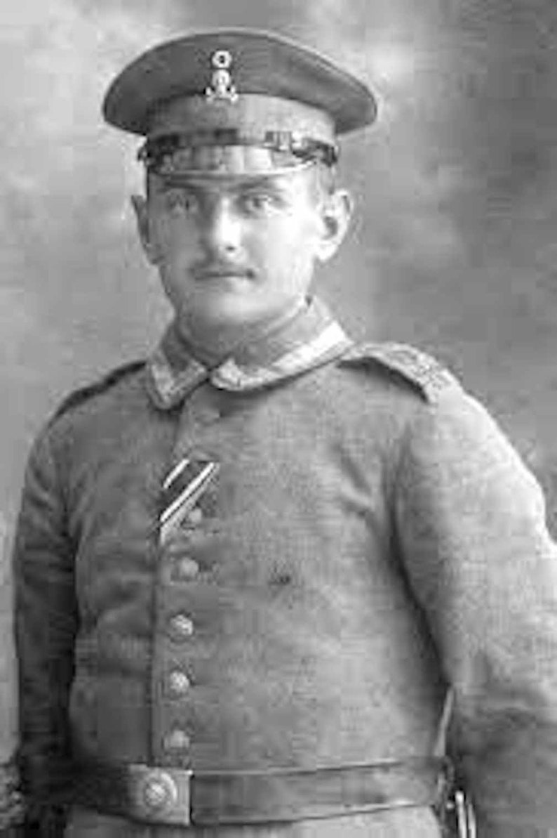 May include: Black and white portrait of a man in a military uniform. He wears a peaked cap with a badge, a button-down jacket with a medal, and a belt. The uniform has a high collar and shoulder epaulettes.