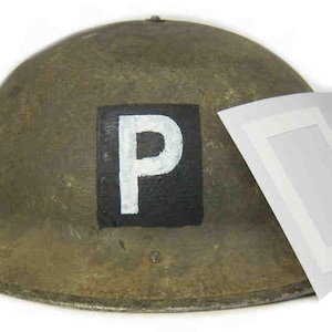 May include: An olive drab military helmet with a white "P" painted on a black square. A sheet of white decals with a similar "P" design is next to the helmet. The helmet has a rounded shape and a brim.
