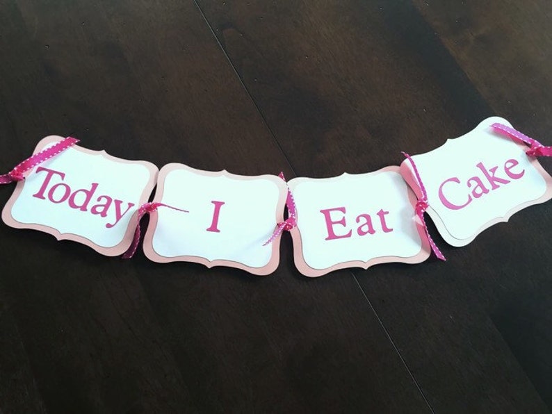K&ouml;nnte beinhalten: Ein rosa-wei&szlig;es Banner mit den Worten "Today I Eat Cake" in rosa Buchstaben. Das Banner ist mit rosa-wei&szlig;em gepunktetem Band verziert.