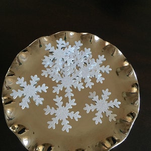 May include: A silver platter with a ruffled edge holds a pile of silver glitter snowflake confetti.