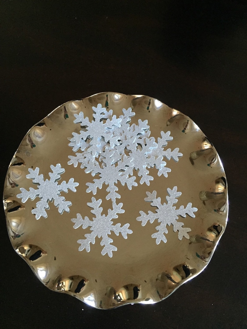 May include: A silver platter with a ruffled edge holds a pile of silver glitter snowflake confetti.