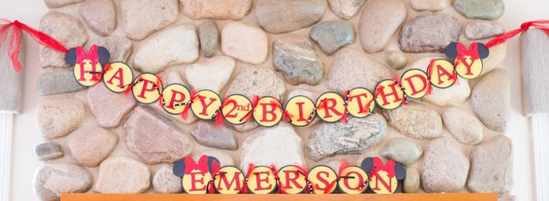 Puede incluir: Una pancarta roja y amarilla con las palabras "Happy 2nd Birthday" y orejas de Minnie Mouse. Debajo de la pancarta, una pancarta con el nombre "Emerson" en rojo y amarillo.
