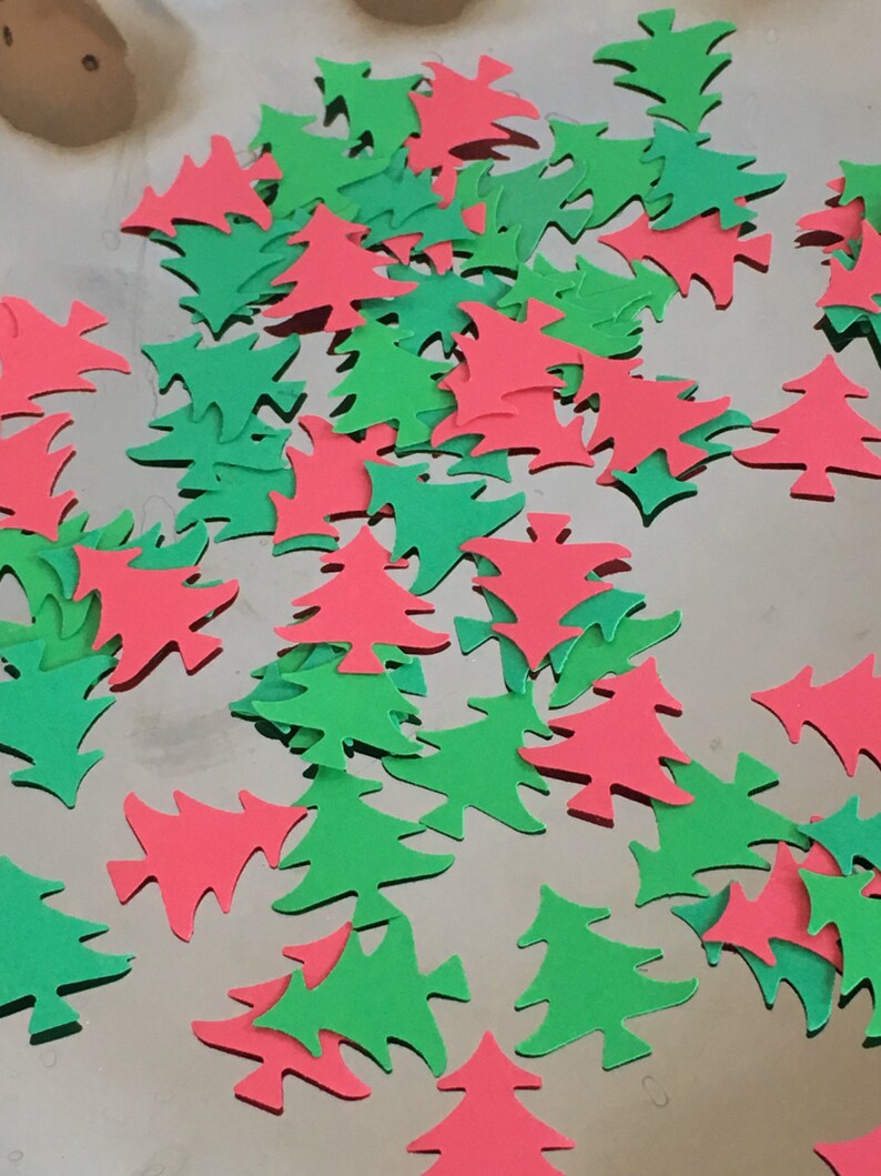 May include: A pile of red and green paper Christmas tree cutouts. The cutouts are scattered on a silver surface.