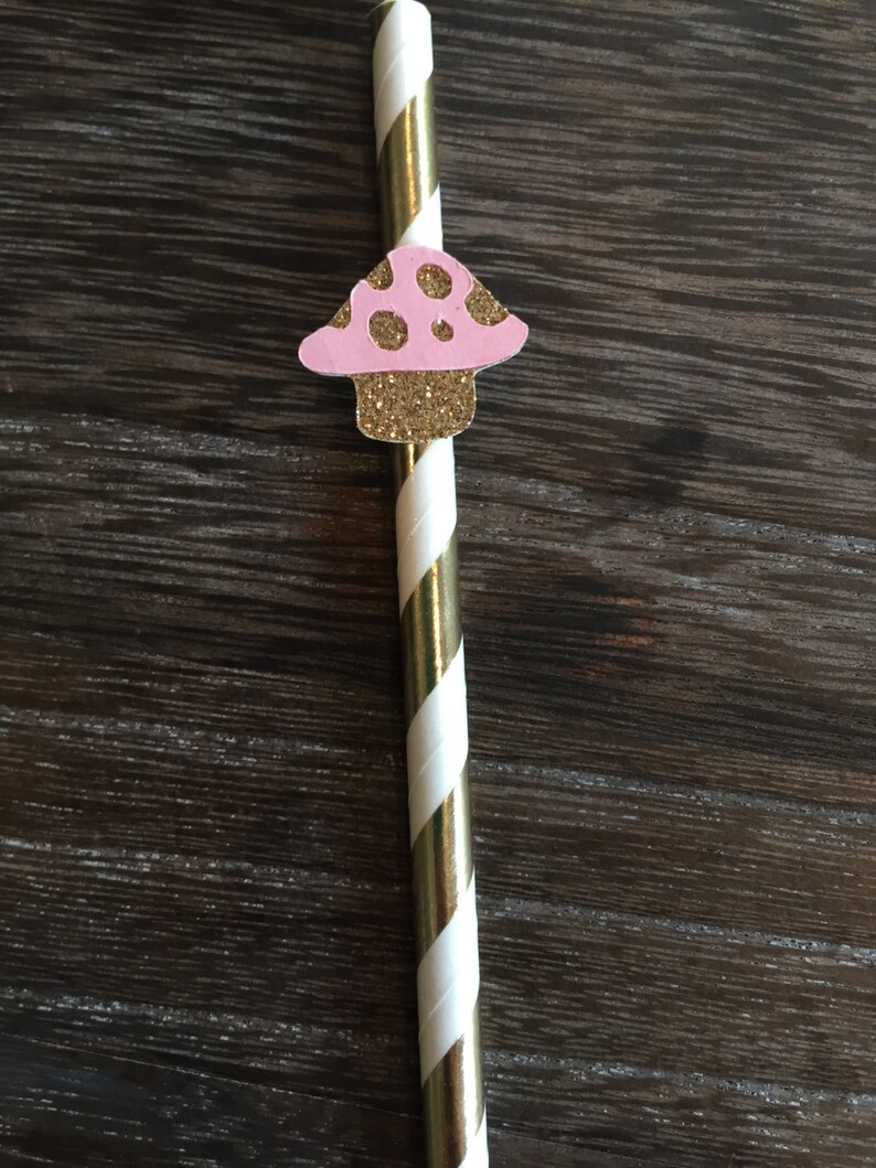 May include: A gold and white striped paper straw with a pink and gold glitter mushroom attached to the top.