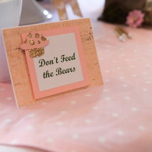 May include: A pink and brown sign with a mushroom graphic and the text "Don't Feed the Bears".