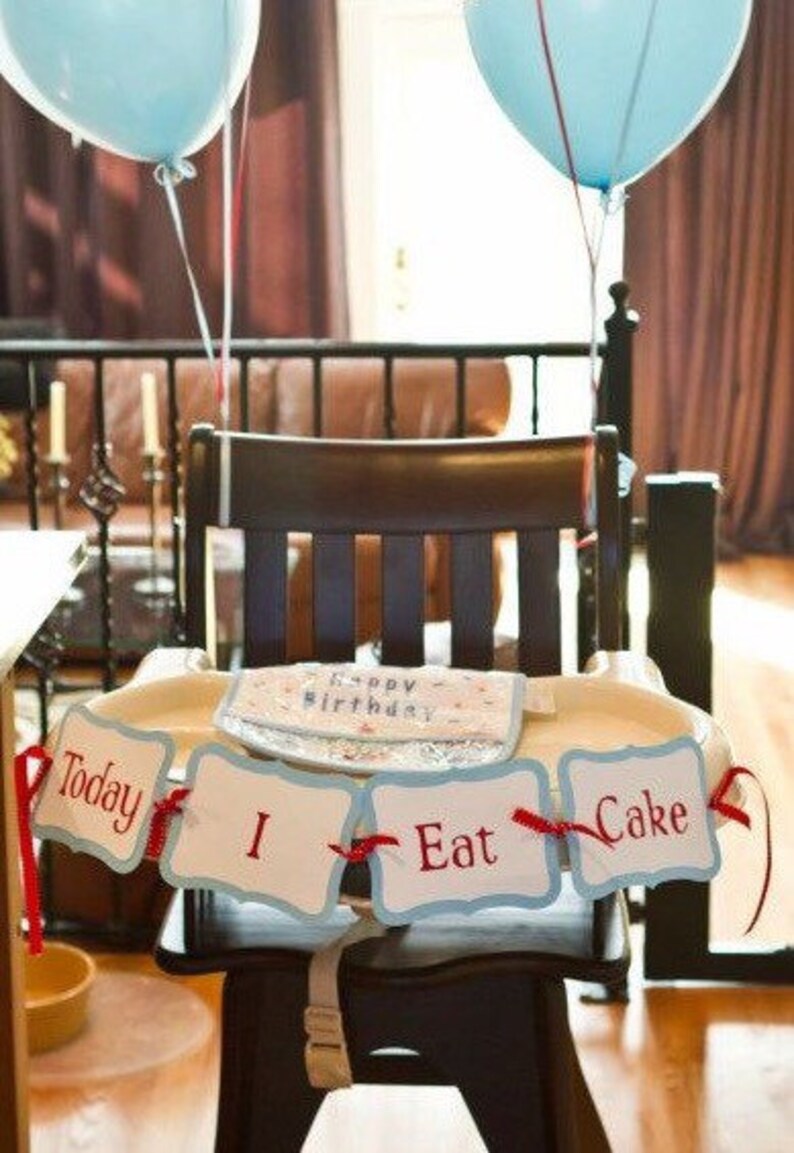 K&ouml;nnte beinhalten: Ein Hochstuhl mit einem blau-wei&szlig;en Banner, auf dem "Today I Eat Cake" steht. Das Banner ist mit rotem Band verziert. Zwei blaue Ballons sind an der R&uuml;ckenlehne des Stuhls befestigt.