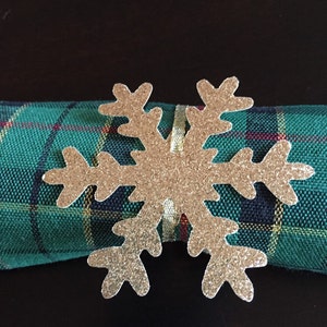 Op de afbeelding: Een servetring in de vorm van een gouden glitter sneeuwvlok op een groen-zwart geruite servet.