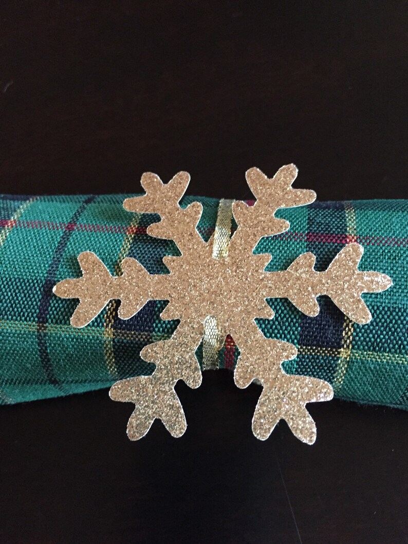 Op de afbeelding: Een servetring in de vorm van een gouden glitter sneeuwvlok op een groen-zwart geruite servet.