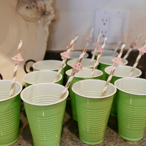 May include: A set of green plastic cups with white rims and pink and white striped straws with mushroom-shaped toppers.
