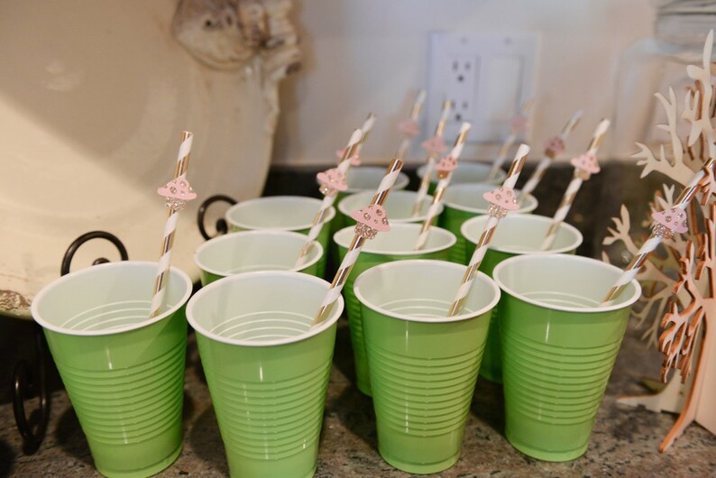 May include: A set of green plastic cups with white rims and pink and white striped straws with mushroom-shaped toppers.