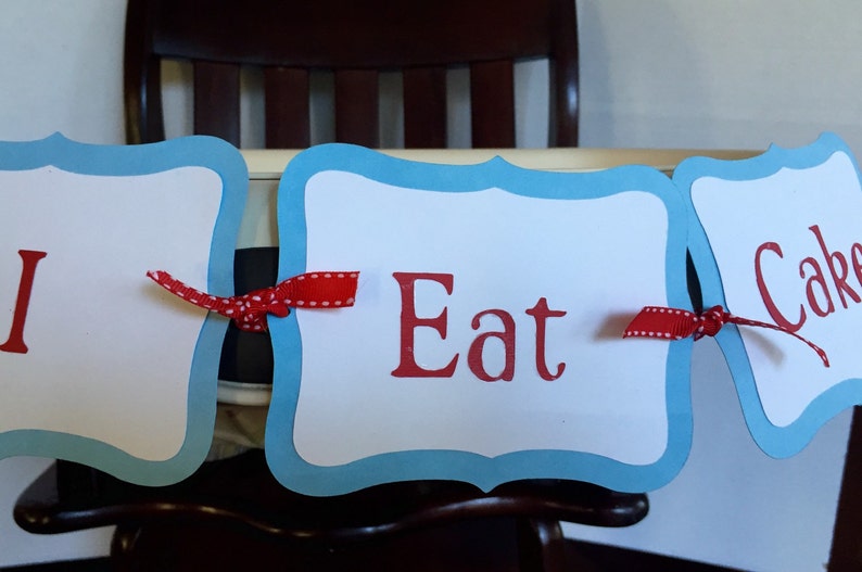K&ouml;nnte beinhalten: Ein blaues und wei&szlig;es Banner mit roten Schleifenb&auml;ndern, auf dem "I Eat Cake" steht.