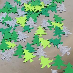 May include: A scattering of green, lime green, and silver glitter Christmas tree confetti. The confetti is made of paper and is perfect for adding a festive touch to any craft project or party.